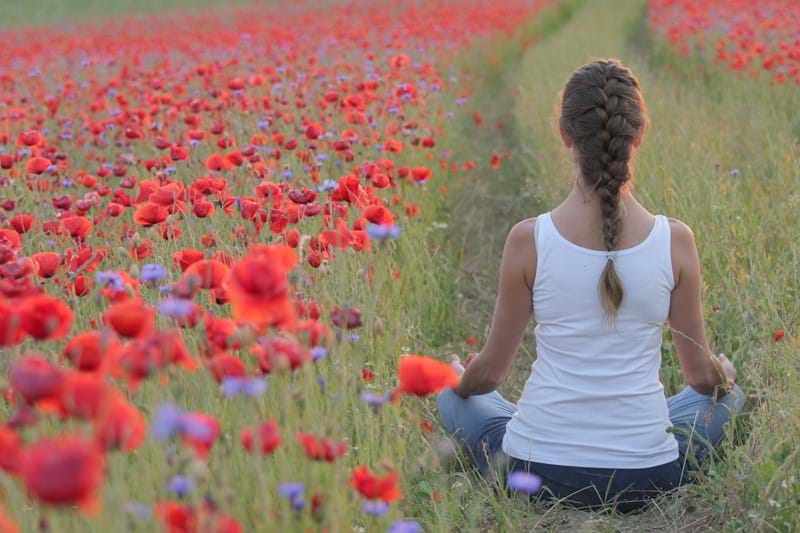 Woman doing yoga in a field of poppy flowers